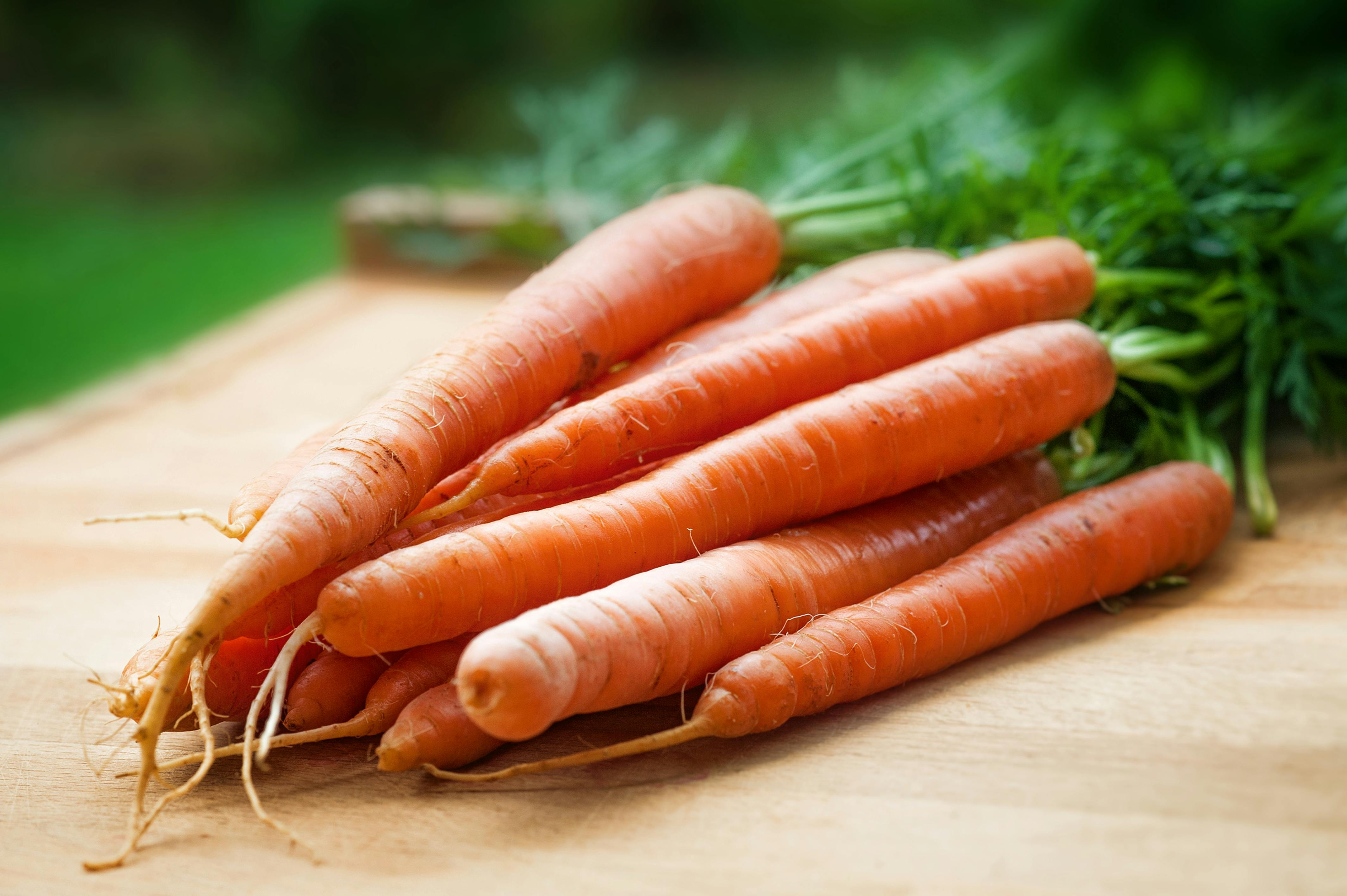 Bunch of carrots on a wooden surface with a blurred green background