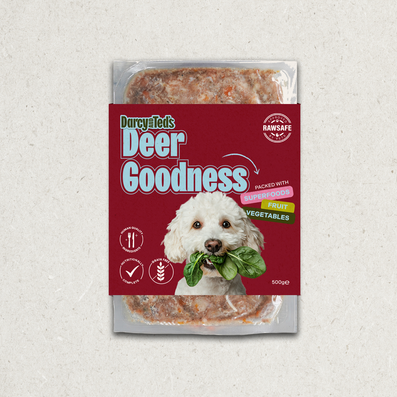 Darcy and ted raw dog food package labeled 'Deer Goodness' with a dog holding greens on a textured gray background