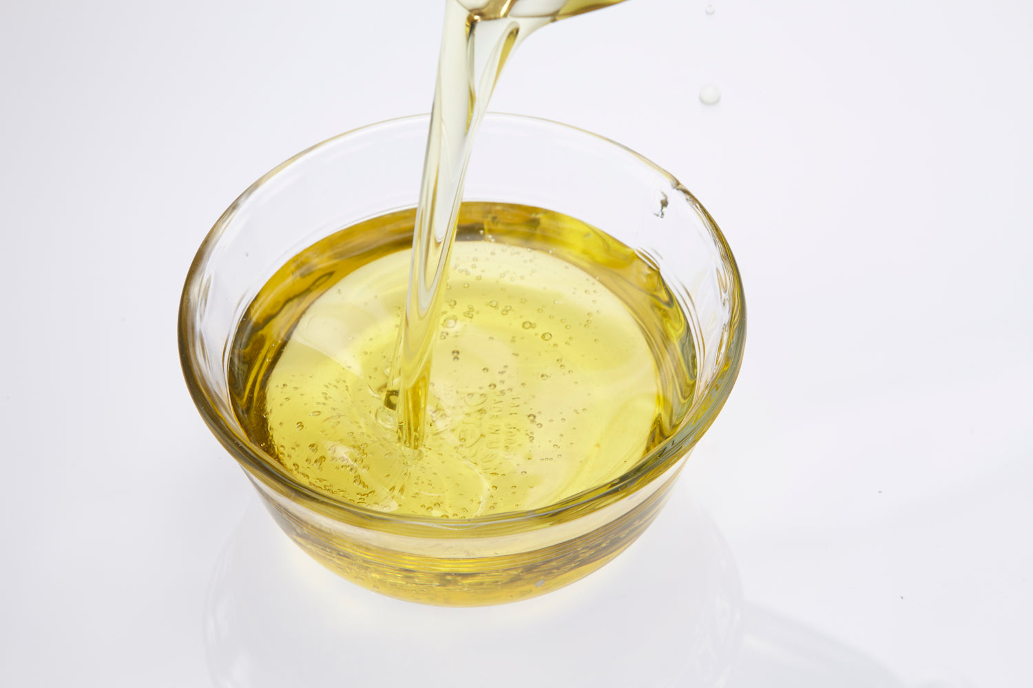 Glass bowl being filled with salmon oil on a white background