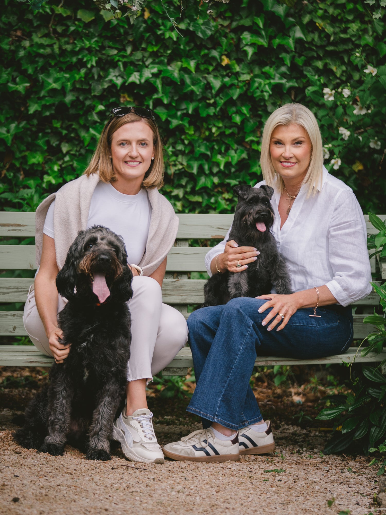 Darcy and Ted's founders, Joanne and Gillian, sitting on a bench with their two dogs, Darcy and Ted, surrounded by greenery.