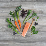Salmon fillet with carrots, spinach, and blueberries on a wooden surface