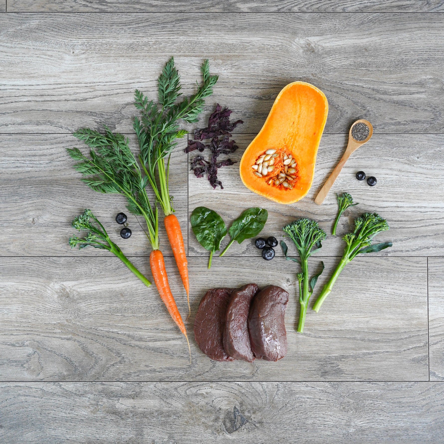 Raw deer meat slices, vegetables, and a butternut squash on a wooden surface