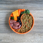 Pet food bowl with loaded lamb, raw meat, carrots, and broccoli on a wooden surface