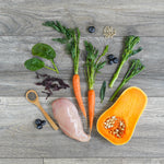 Assorted vegetables and a piece of chicken on a wooden surface