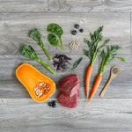 Assorted ingredients including a butternut squash, carrots, and greens on a wooden surface